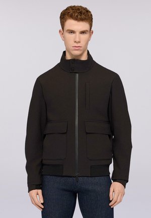 Giacca nera con colletto alto, zip frontale, due ampie patte per le tasche e polsini a coste. Realizzata in un materiale liscio e strutturato.
