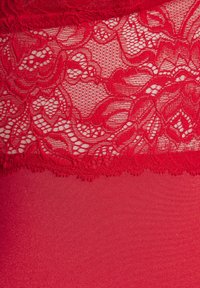 Red lace top features floral patterns with a scalloped edge, paired with a smooth red fabric bottom. Overall, a textured and vibrant design.