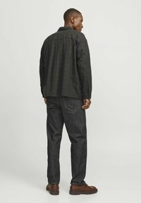 Cămașă cu patrate negre, cu mâneci lungi, asociată cu blugi denim închis. Setul are o croială lejeră și detalii hardware minime.
