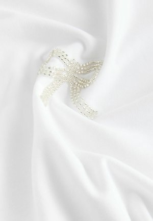 Tissu blanc avec un motif texturé, présentant un design de nœud perlés dans une couleur neutre subtile. Texture douce et lisse.