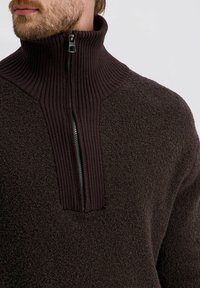 Bruine fleece pullover met een geribde hoge kraag. Voorzien van een halve rits en een textuurstof, wat een gezellige uitstraling creëert.