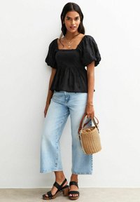 Black puff-sleeve top with textured floral patterns, paired with light blue wide-leg jeans and a woven handbag. Black platform sandals included.