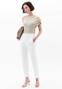 Beige off-the-shoulder top med samlede ærmedetaljer, parret med skræddersyede hvide bukser og beige strophæle. Guld clutch-taske.