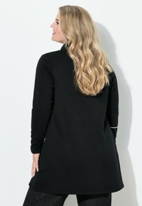 Czarny sweter na długi rękaw wykonany z miękkiego materiału, o prostym kroju, z kołnierzem i białym akcentem na dole.