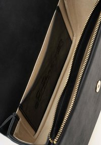 Zwarte leren handtas interieur met een lichtbeige voering, een ritsvak en een insteekvak met reliëfbranding.