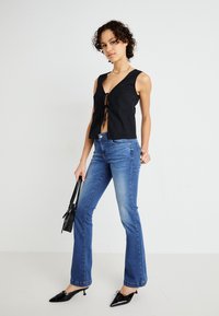 Černý upnutý crop top s detailem zavázání vpředu, spárovaný s modrými džíny s mírným zvýšením a černými botami na podpatku s ostrou špičkou.