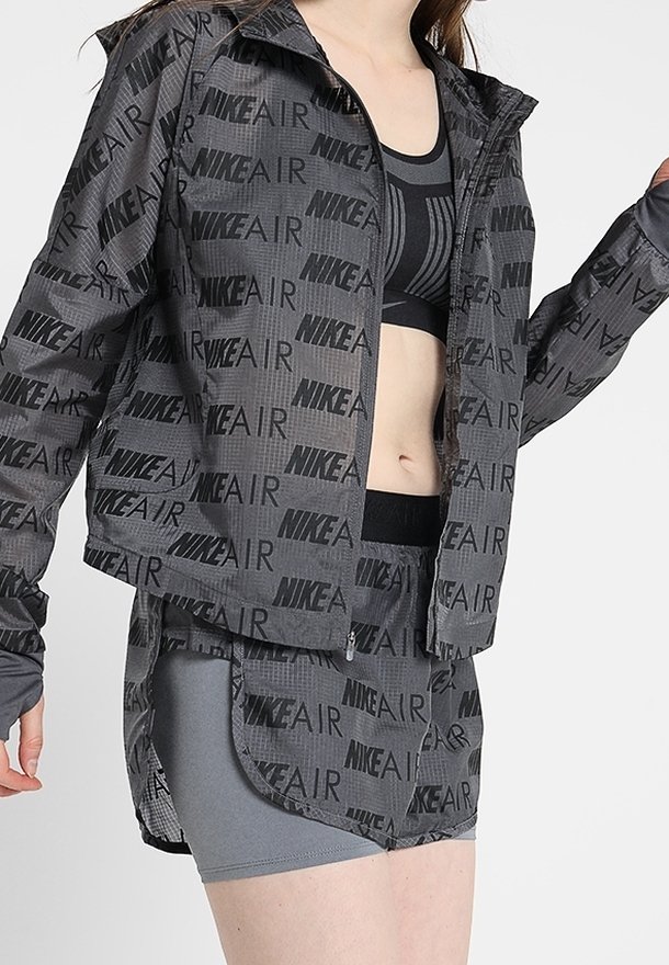 Ensemble de vêtements de sport gris comprenant une veste à zip avec un imprimé répété "NIKE AIR", un design cropped, et une jupe ajustée assortie.