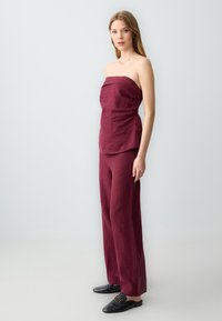 Bordeaux linnen strapless top met zijrimpeling, gecombineerd met een wijde broek. De look heeft een soepele textuur en een minimalistisch ontwerp.