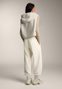 Fehér, kapucnis, rövidített fleece kapucnis felső, bő szabású, krém színű melegítőnadrággal és világos színű cipővel párosítva, kényelmes öltözetet alkotva.