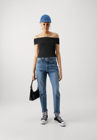 Svart off-the-shoulder topp, blå denimjeans, svarte sneakers og en liten svart håndveske. Glatt stoff og avslappet passform.
