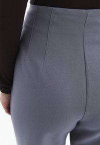 Grå skräddarsydda byxor med en slät yta, med subtila veck och hög midja. Närbild som fokuserar på baksidan.