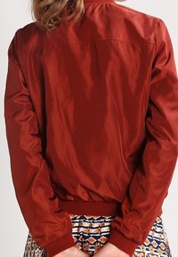 Rote Nylon-Bomberjacke mit glatter Textur, gerippten Bündchen und Saum sowie einem schlichten Design. Die Rückseite zeichnet sich durch eine saubere Verarbeitung ohne Verzierungen aus.