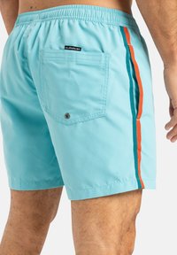 Shorts de bain bleu clair avec une taille élastique, des rayures latérales en orange et en vert émeraude, et une poche arrière avec une fermeture à pression.