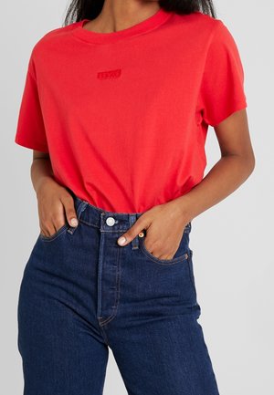 Czerwona bawełniana koszulka z okrągłym dekoltem i wytłoczonym logo "Levi's" na piersi, zestawiona z ciemnoniebieskimi dżinsami z wysokim stanem.