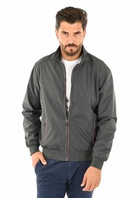 Giubbotto bomber grigio con zip davanti, polsini a costine e due tasche laterali. Presenta cuciture in contrasto e colletto rialzato.