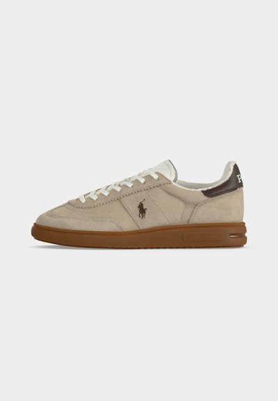 Μπεζ σουέτ sneaker χαμηλής κοπής με καφέ σόλα, λευκά κορδόνια, σκουροκάστανο ταμπά στο τακούνι και μικρό σκουρόχρωμο λογότυπο στο πλάι.