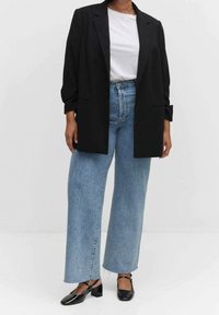 Musta suureneva bleiseri valge T-särgi peal, koos helesiniste kõrge vöökohaga laiad püksid ja mustade terava ninaga kingadega.