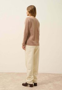 Brązowy, teksturowany sweter o luźnym kroju, zestawiony z jasnobeżowymi, szerokimi spodniami i ciemnymi botkami na obcasie, widziany z tyłu.