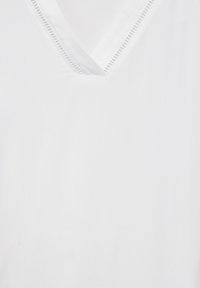 Blusa di cotone bianca con scollatura a V, dotata di una delicata bordatura e una superficie liscia e morbida. Design minimalista senza motivi o dettagli.