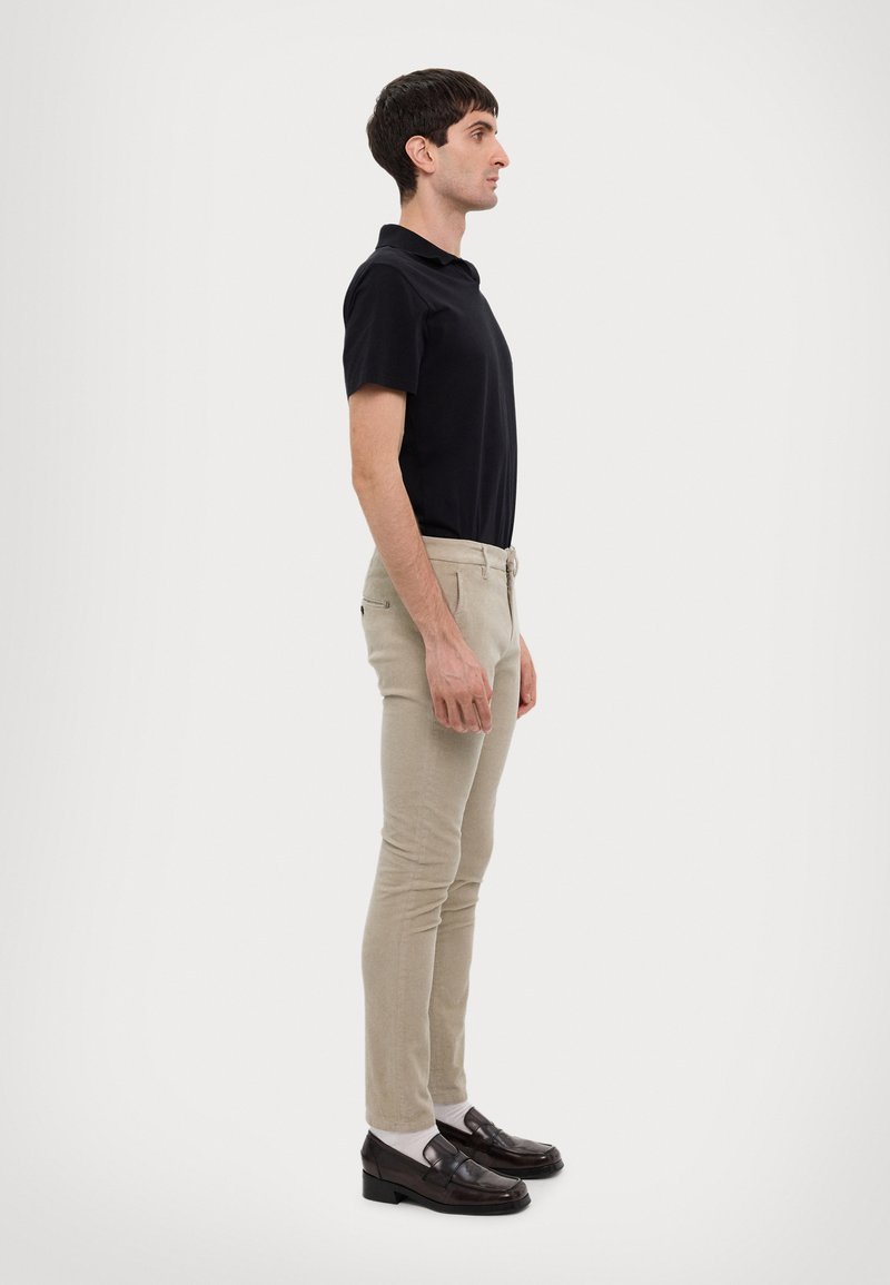 Polo nero a maniche corte, pantaloni beige slim-fit e mocassini scuri. Design semplice, forma aderente, senza pattern visibili o loghi.