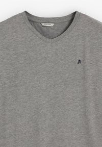 Graues V-Ausschnitt-T-Shirt aus weichem Stoff mit kurzen Ärmeln. Mit einem kleinen marineblauen Totenkopf-Logo auf der linken Brust. Minimalistisches Design.