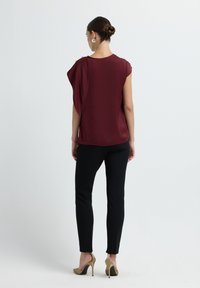 Top bordeaux con design a spalla asimmetrica abbinato a pantaloni neri aderenti. Scarpe con tacco di un colore chiaro completano l'outfit.