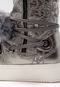 Botte de sneaker grise métallique avec broderies florales, détail de pompon, fermeture éclair sur le côté et semelle blanche épaisse.