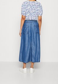 Blommig kortärmad topp i ljusa färger, matchad med en lång blå denimkjol med två bakfickor, bärs med vita sneakers.