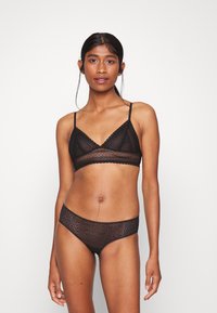 Svart blonde bralette med justerbare stropper, med en bølget kant og semi-transparent tekstur, kombinert med matchende blonde truser.