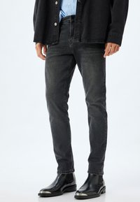 Jeans de mezclilla negros de corte slim, con un clásico diseño de cinco bolsillos y un ligero desgaste, combinados con botas negras hasta el tobillo.