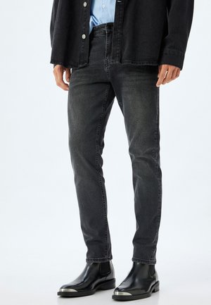 Sorte denimjeans med en slank pasform, der har et klassisk fem-lomme design og diskret fald, parret med sorte ankelstøvler.