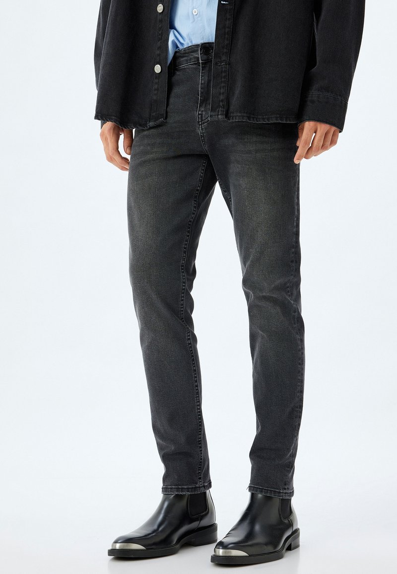 Jeans de mezclilla negros de corte slim, con un clásico diseño de cinco bolsillos y un ligero desgaste, combinados con botas negras hasta el tobillo.