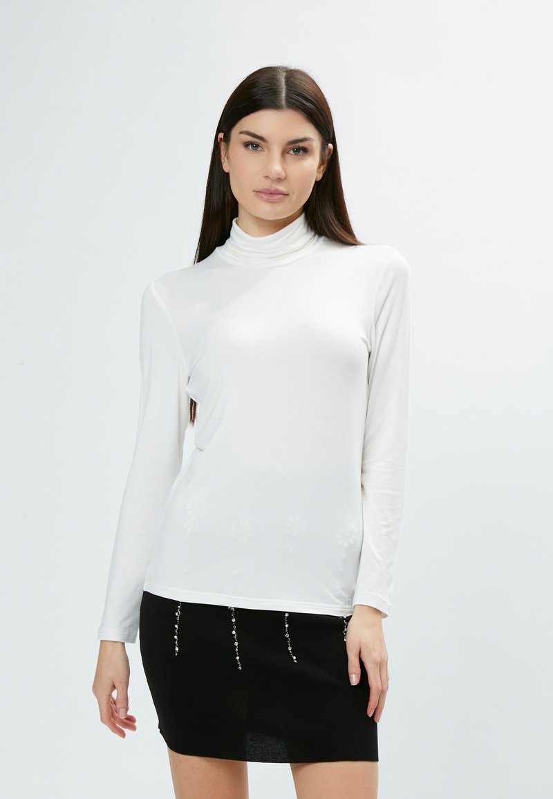Weißes Langarm-Turtleneck-Oberteil aus glattem Stoff, kombiniert mit einem schwarzen Minirock, der mit Perlenakzenten am Saum verziert ist.