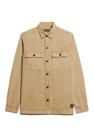 Camisa de botón color tostado claro con dos bolsillos frontales, botones negros y detalles cosidos. Ajuste entallado con cuello y etiqueta lateral.