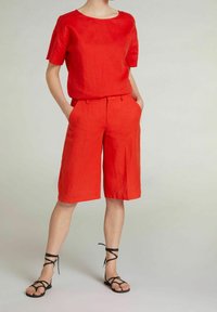 Rød linned T-shirt med korte ærmer parret med røde linned shorts, der har en løs pasform og forlommer. Sorte sandaler med stropper fuldender outfittet.