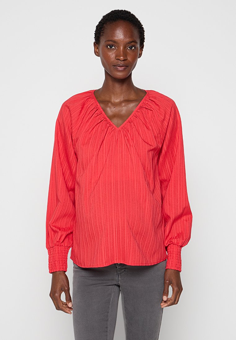 Blusa roja de manga larga con escote en V, que presenta rayas verticales texturizadas y detalles fruncidos en el escote y en los puños.