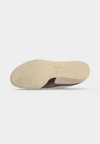 Semelle de chaussure en caoutchouc beige avec de petites prises rondes et un petit logo rose au centre, montrant partiellement le côté de la chaussure marron clair.