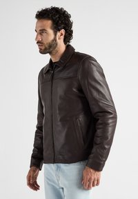 Dunkelbraune Lederjacke mit Kragen, Frontreißverschluss und seitlichen Taschen. Glatte Textur mit minimalen Nähdetails. Lässiges Design.