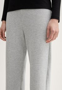 Pantalones de chándal gris claro hechos de tela suave, con un diseño de pierna recta y una textura sutil, combinados con una camiseta negra de manga larga.