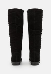 Botas altas de ante negras con tacones planos y cremalleras traseras, mostradas desde la parte trasera sobre un fondo blanco.