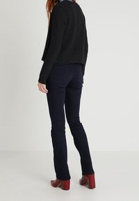 Černá texturovaná zkrácená bunda, tmavě modré rozšířené džíny a červené lodičky na podpatku. Bunda má volný střih; džíny mají zadní kapsy.