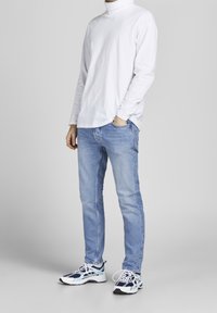 Vit långärmad polotröja, ljusblå jeans och blå sneakers. Polotröjan har en slät yta; jeansen har en klassisk passform; sneakers med en flerfärgad design.