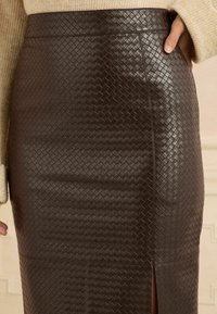 Fustă din piele sintetică maro cu o textură împletită, având un design ajustat și o fanta laterală, care îi pune în evidență aspectul structurat.