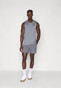 Pánský atletický outfit zahrnující šedé tílko bez rukávů a šedé šortky, doplněný bílými teniskami. Jednoduchý design, lehký materiál.