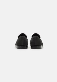 Mocasines de tela negra con puntera redonda, tacón bajo y diseño minimalista. Textura suave y detalle de costura sutil en la parte superior.