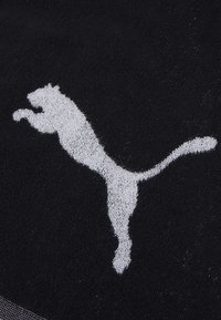 Tissu noir avec un logo Puma brodé blanc bien en évidence, représentant un chat qui saute avec des détails et une texture clairs.