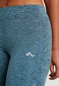 Granatowe legginsy z mieszanką tkanin mają elegancki krój z małym logo przy dolnej krawędzi. Materiał ma teksturowany wzór oraz dopasowany krój.