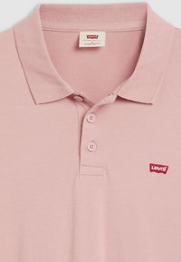 Polo rose clair en coton. Dispose d'un col classique, d'une patte de boutonnage à trois boutons et d'un petit logo Levi's rouge sur la poitrine.