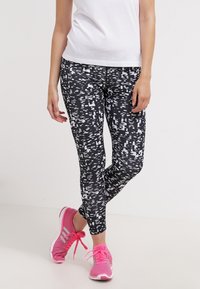 Mustat ja valkoiset kuviolliset leggingit, joissa on abstrakti muotoilu, valmistettu joustavasta kankaasta, yhdistettynä kirkkaan pinkkeihin urheilukenkiin.