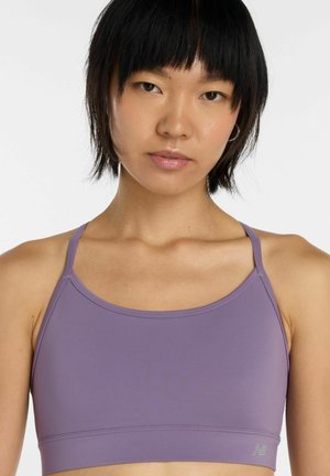 Ung kvinde med kort sort hår iført en lyse lilla sports-bh, der kigger direkte ind i kameraet mod en ensfarvet hvid baggrund.